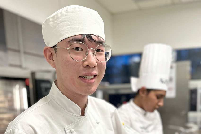 Benjamin Kim in white chef clothes and wearing glasses, working in a professional kitchen