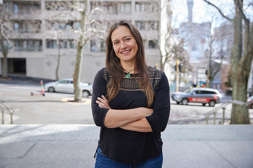 Associate Professor Antje Deckert standing on a street, arms folded and smiling.