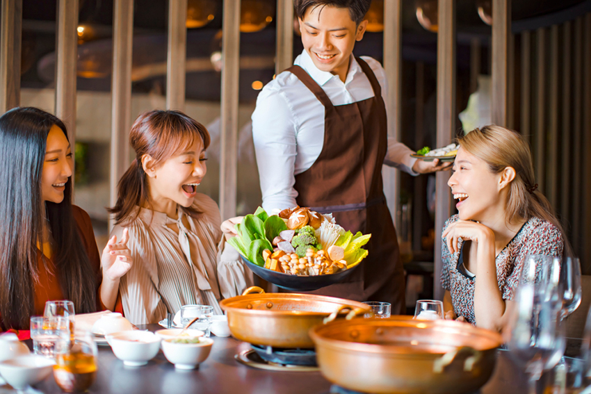 Waiter bring vegetables for hot pot and serving group of friends in restaurant.