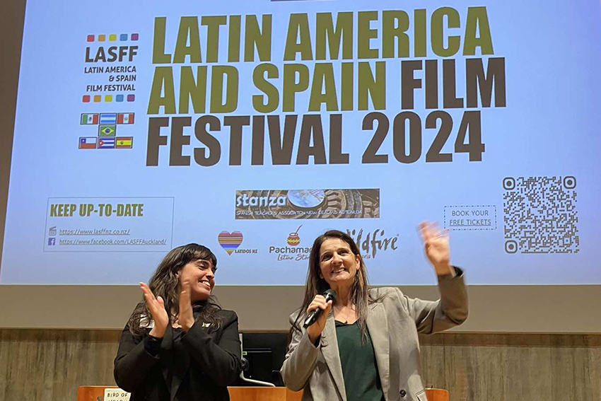 Elba Ramirez and Gloria Vazquez stand clapping in front of a sign promoting the LASFF 2024.