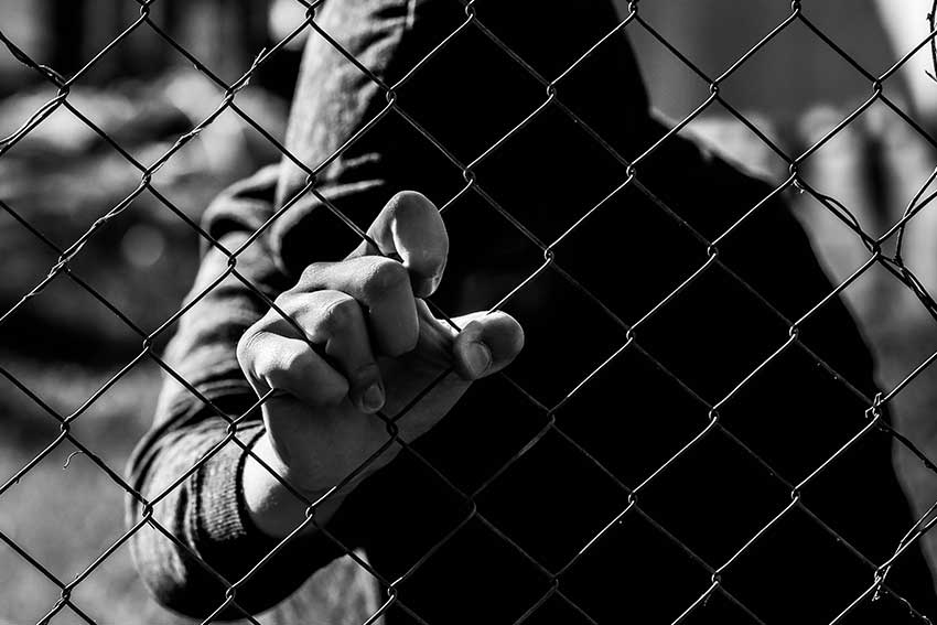 Young unidentifiable teenage boy holding the wired garden at the correctional institute in black and white, conceptual image of juvenile delinquency, focus on the boys hand.